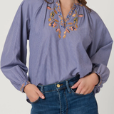 Woman wearing a blue blouse with floral embroidery and blue jeans on a white background