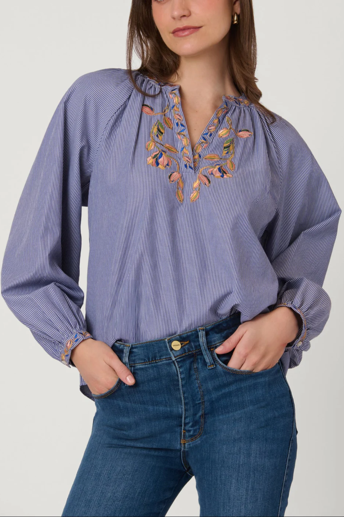 Woman wearing a blue blouse with floral embroidery and blue jeans on a white background