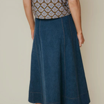 A person shown from the back wearing a dark blue denim midi skirt with a patterned top, standing against a plain beige studio background.