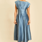 A woman modeling a light blue midi dress with a gathered waist and cap sleeves, standing against a solid beige background.