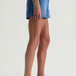 Person wearing a blue denim skirt and white sandals on a plain background