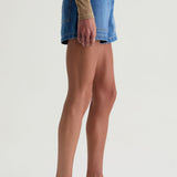 Person wearing a blue denim skirt and white sandals on a plain background
