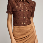 A model wearing a brown lace short-sleeve button-up blouse with ruffled sleeves and a tan faux-suede wrap mini skirt, photographed against a light gray studio background.