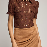 A model wearing a brown lace short-sleeve button-up blouse with ruffled sleeves and a tan faux-suede wrap mini skirt, photographed against a light gray studio background.