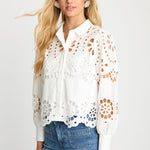 Woman wearing a white lace blouse with cut-out patterns on a plain background