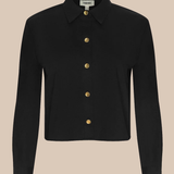 A black long-sleeve collared shirt jacket with gold buttons, displayed on a solid beige background.