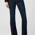 A model wearing dark blue flare jeans, a black long-sleeve top, and black pointed-toe heels, standing against a light gray studio background.