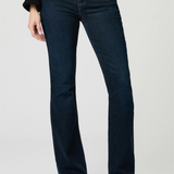 A model wearing dark blue flare jeans, a black long-sleeve top, and black pointed-toe heels, standing against a light gray studio background.