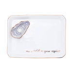 A white rectangular ceramic tray with rounded corners, featuring a raised 3D oyster shell design in the top-left corner and the phrase 'the world is your oyster' in rose gold script along the bottom edge.