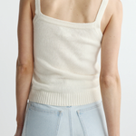 Person wearing a cream-colored knit tank top and light blue jeans on a white background