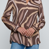 Model wearing a long-sleeve abstract print blouse in warm neutral tones paired with blue denim.