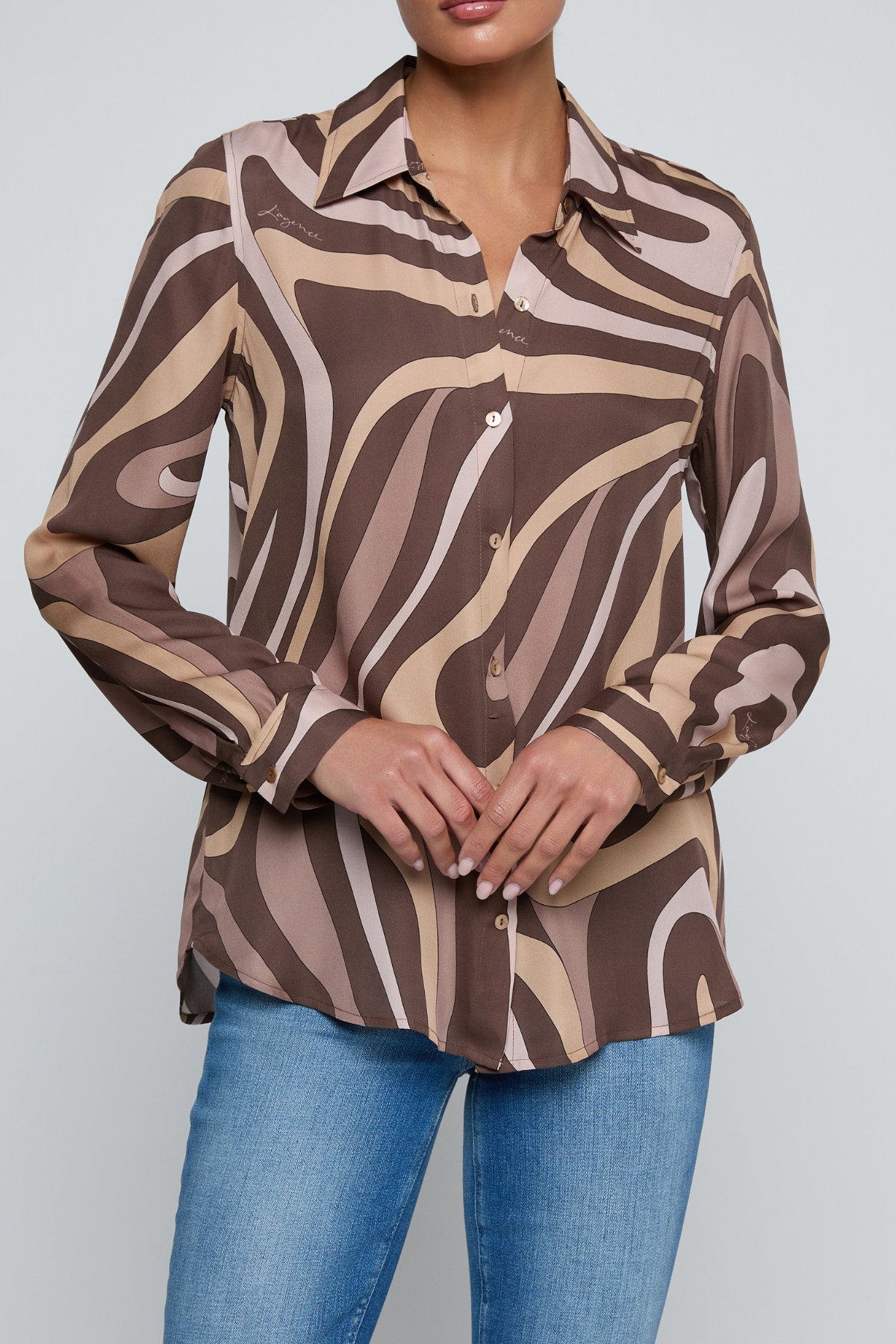 Model wearing a long-sleeve abstract print blouse in warm neutral tones paired with blue denim.