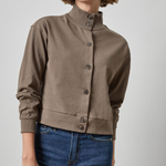 Woman wearing a brown jacket and blue jeans on a plain background