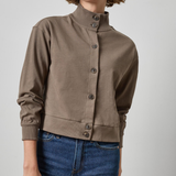 Woman wearing a brown jacket and blue jeans on a plain background