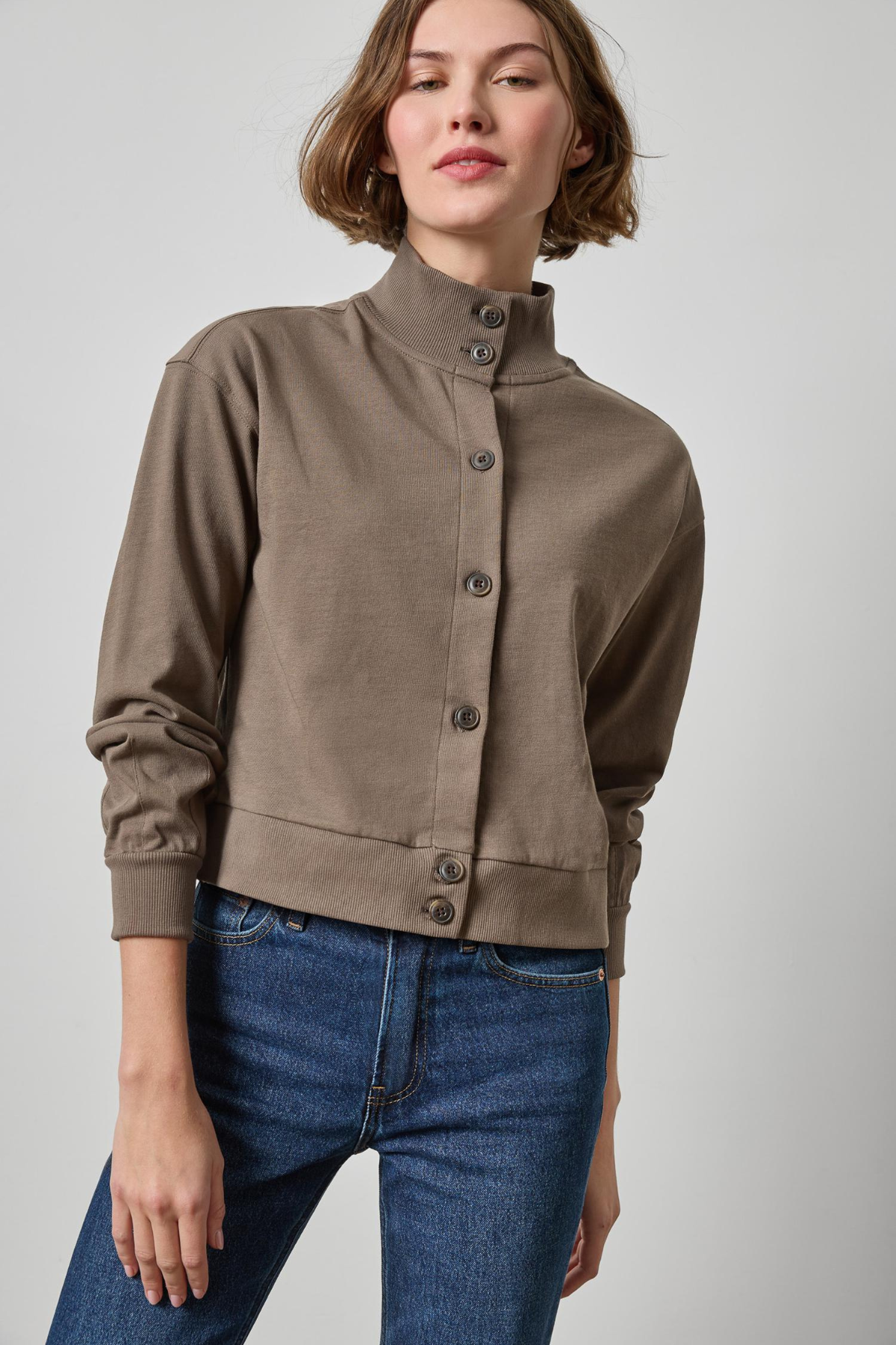 Woman wearing a brown jacket and blue jeans on a plain background