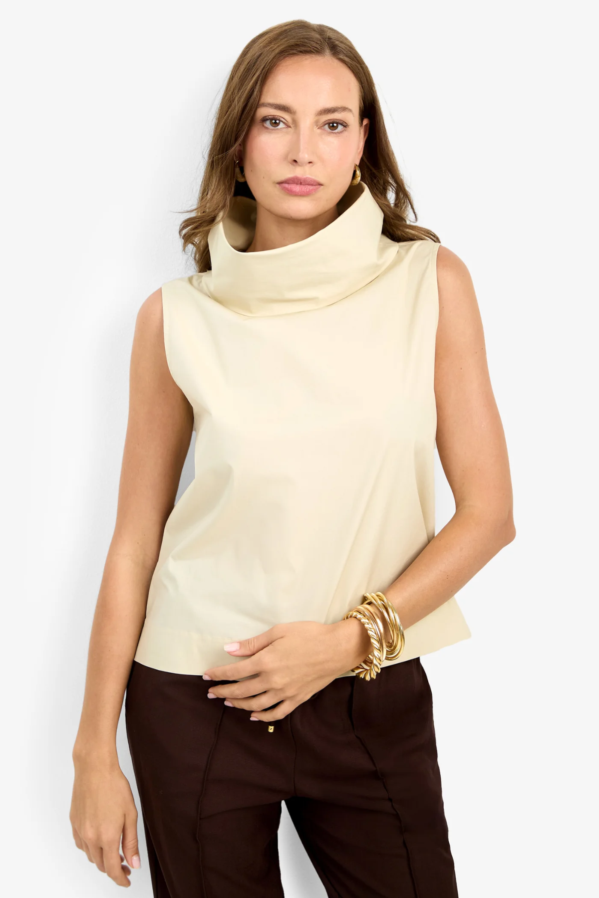 Woman wearing a beige sleeveless top and brown pants on a white background