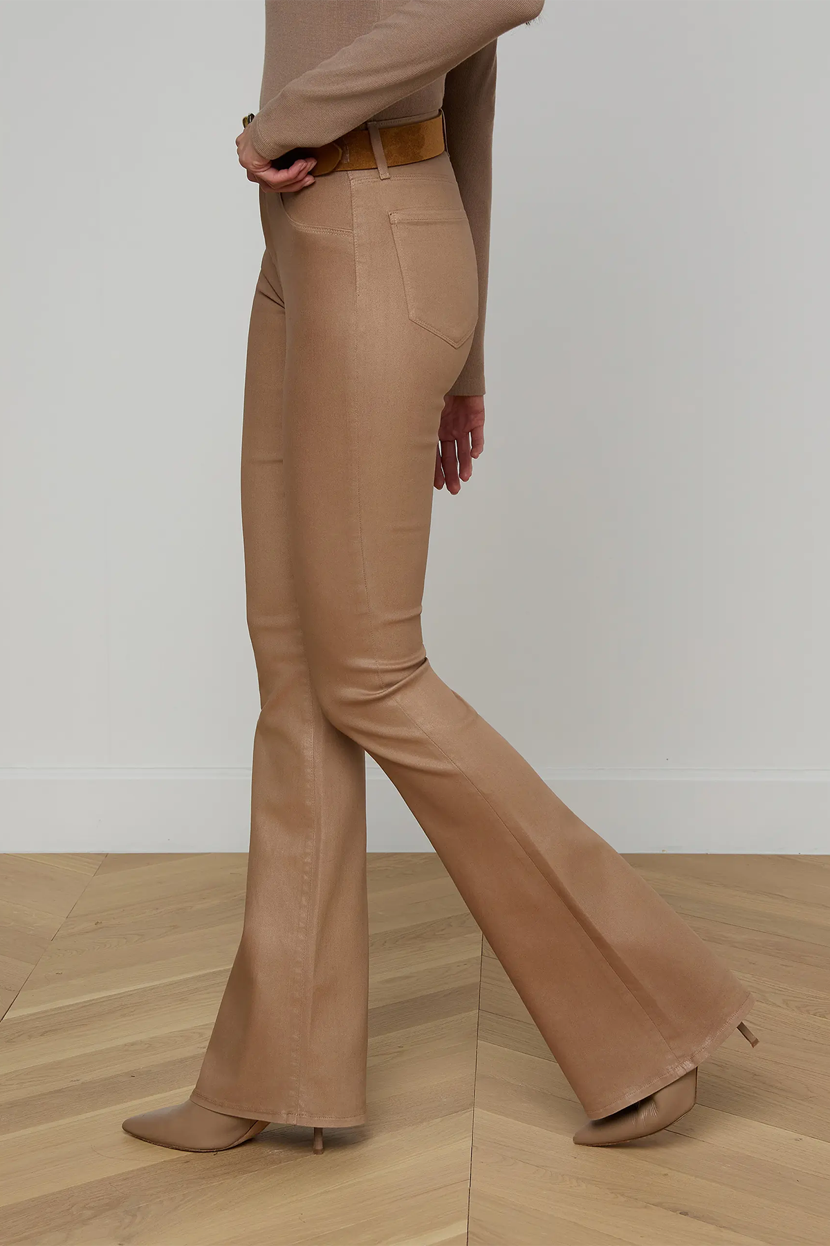 Person wearing beige flared pants on a wooden floor with a white wall background