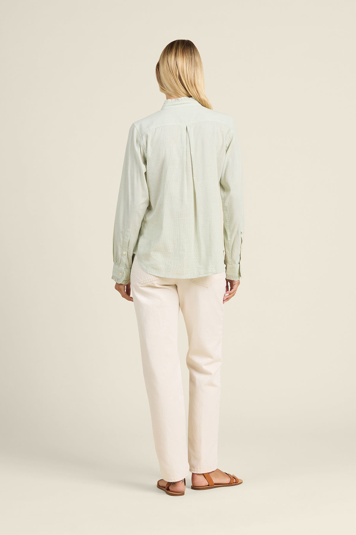 Person wearing a light green shirt and white pants on a beige background