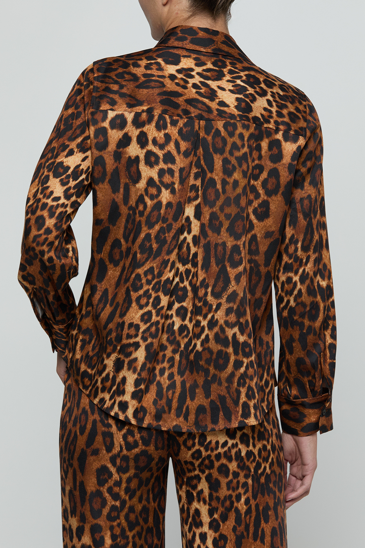 A person shown from the back wearing a leopard-print long-sleeve shirt and matching pants against a light gray studio background.