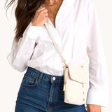 Woman wearing a white blouse and blue jeans with a cream-colored handbag.