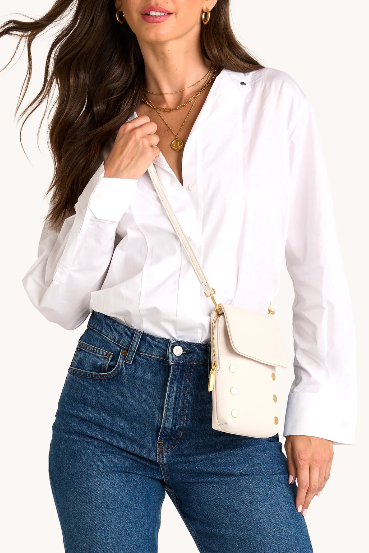 Woman wearing a white blouse and blue jeans with a cream-colored handbag.