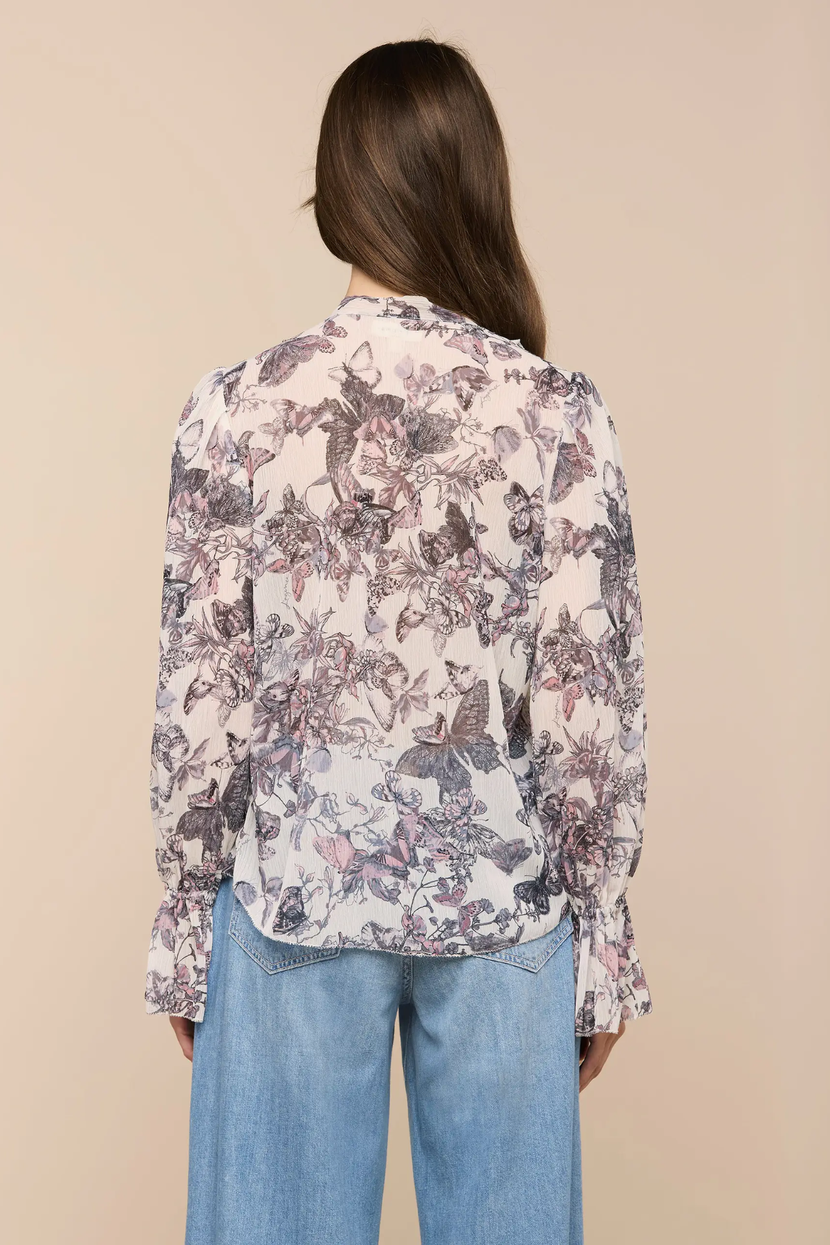 Person wearing a floral blouse and blue jeans on a beige background