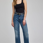 A woman modeling a pair of medium-wash blue wide-leg jeans with a black tank top and black pointed-toe heels, standing against a light gray studio background.