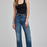 A woman modeling a pair of medium-wash blue wide-leg jeans with a black tank top and black pointed-toe heels, standing against a light gray studio background.