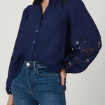 Woman wearing a navy blue blouse with lace sleeves and blue jeans on a light gray background