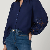 Woman wearing a navy blue blouse with lace sleeves and blue jeans on a light gray background