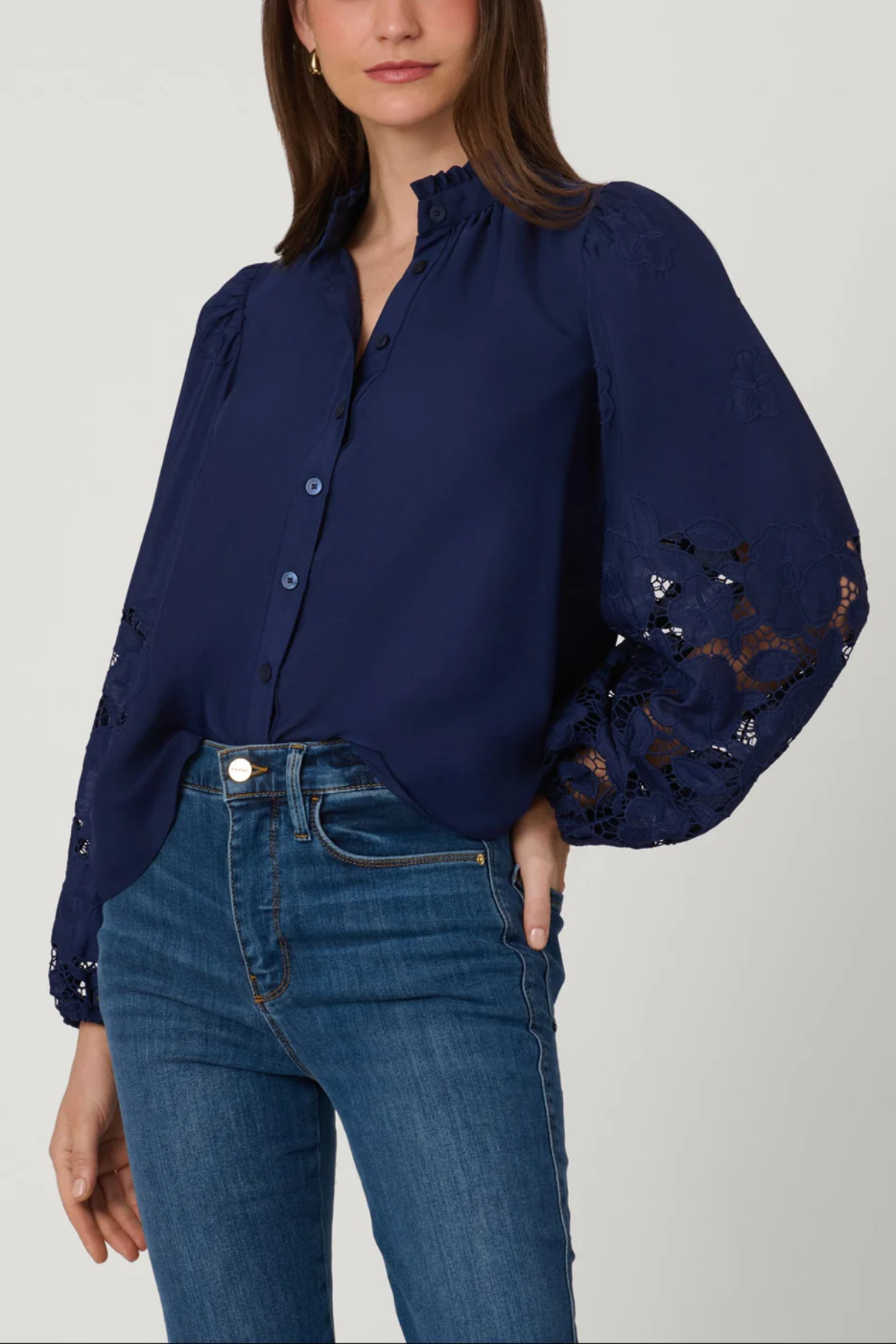 Woman wearing a navy blue blouse with lace sleeves and blue jeans on a light gray background