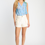 Woman wearing a light blue sleeveless top and white shorts on a white background
