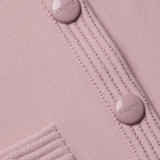 Close-up of a pink textured fabric with buttons and visible branding.