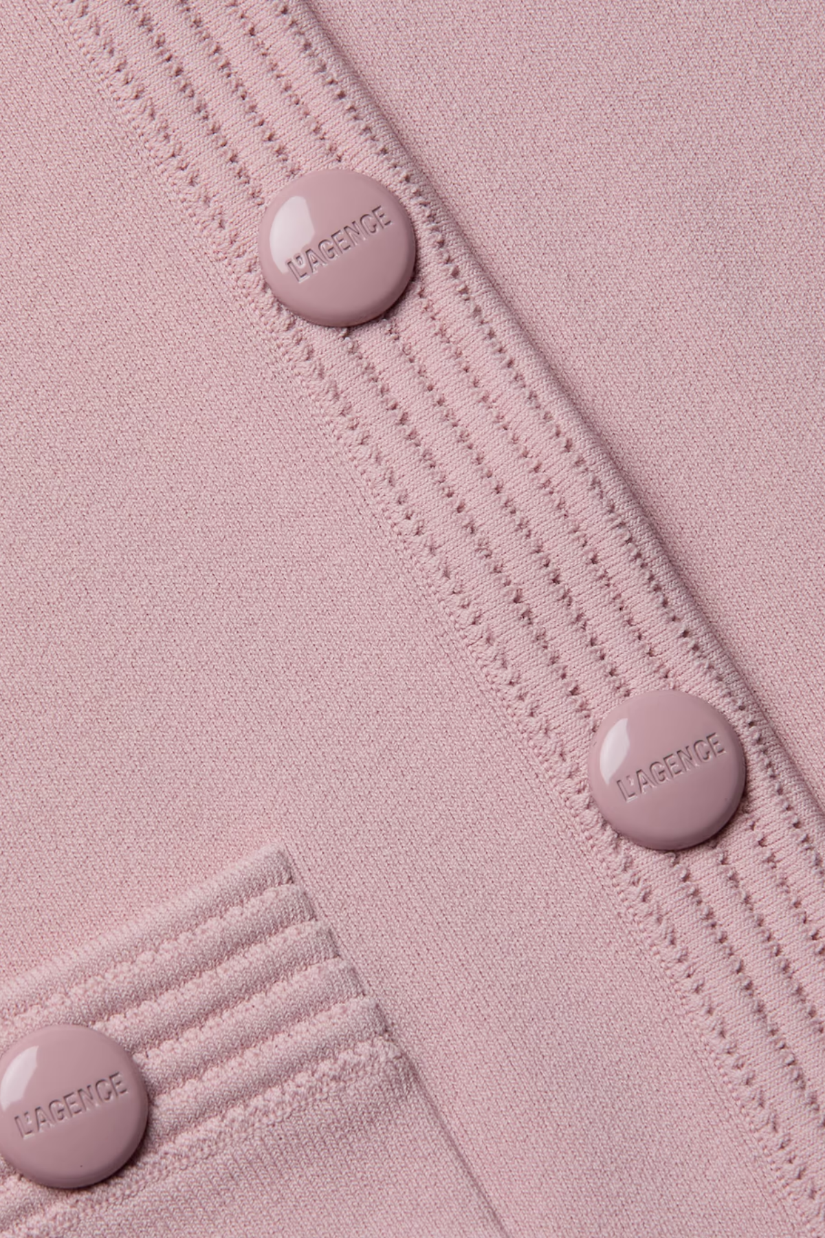 Close-up of a pink textured fabric with buttons and visible branding.