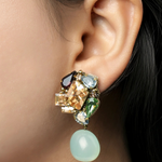 A close-up of a model's ear wearing a statement dangle earring with multiple colorful gemstones and a light green bead drop.