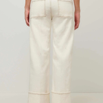 A person shown from the back wearing off-white wide-leg cropped jeans with rolled cuffs and black flats, against a plain light gray studio background.