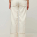 A person shown from the back wearing off-white wide-leg cropped jeans with rolled cuffs and black flats, against a plain light gray studio background.
