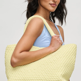 Woman holding a light yellow textured tote bag against a plain background