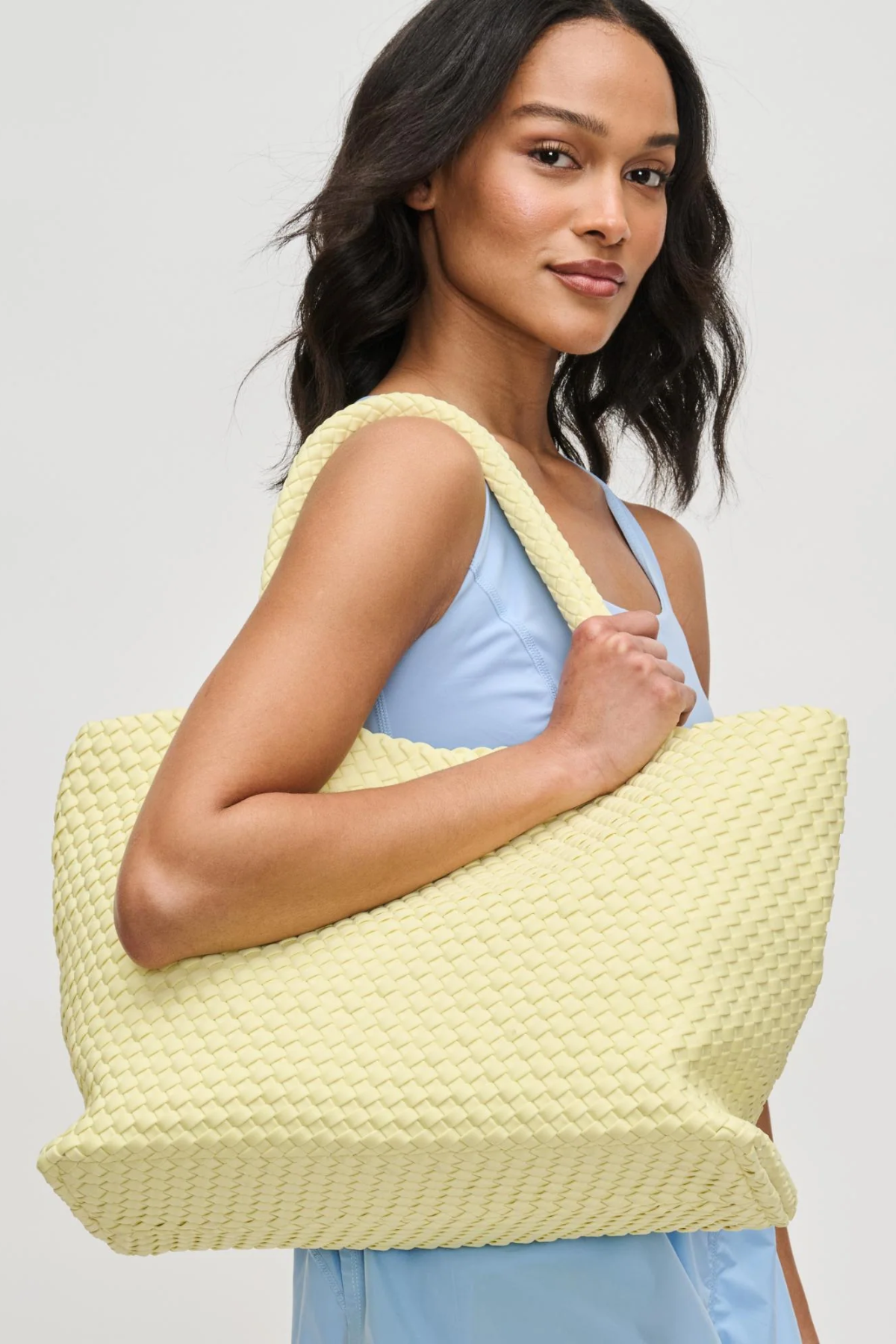 Woman holding a light yellow textured tote bag against a plain background