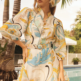 Woman in a colorful floral outfit standing by a pool with palm trees in the background