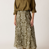 Model wearing printed skirt with a green/khaki shirt on an off white background.
