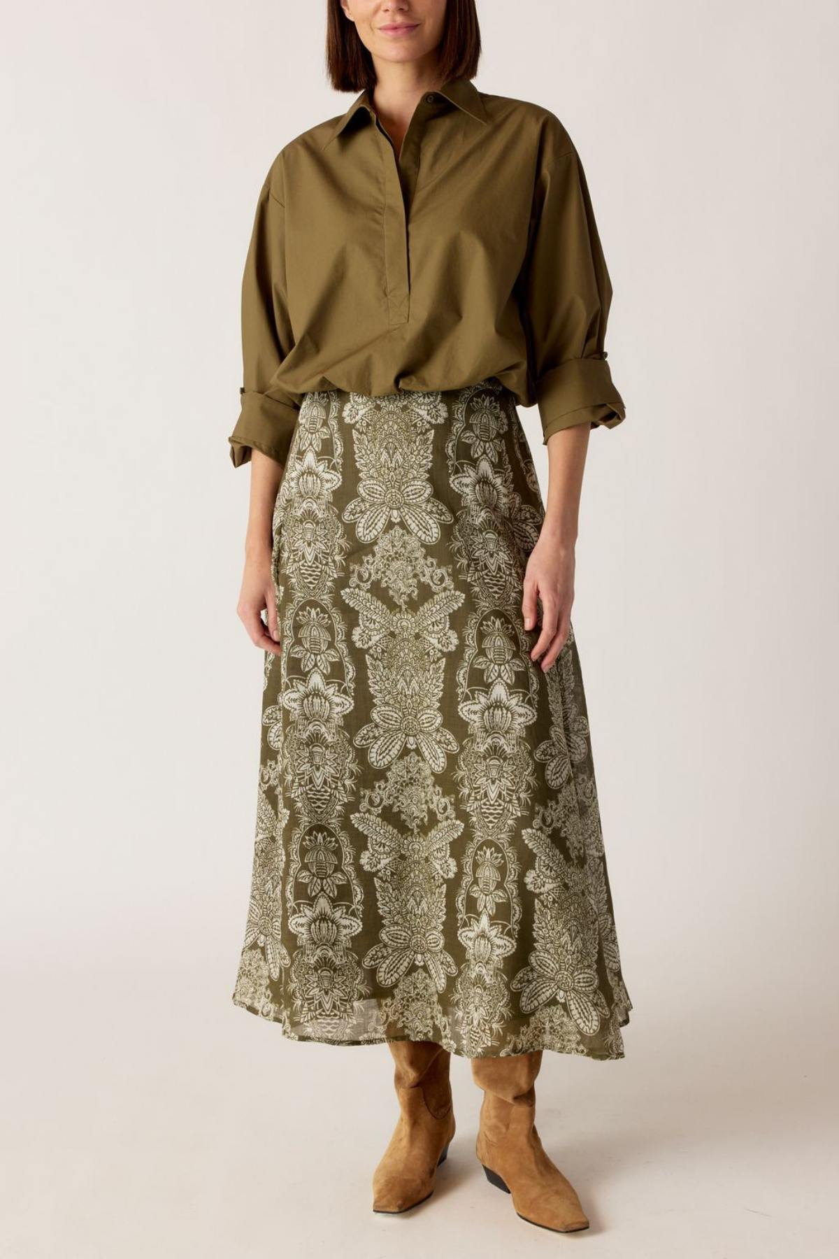 Model wearing printed skirt with a green/khaki shirt on an off white background.