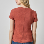 Woman wearing a rust-colored short-sleeve top and blue jeans on a plain background