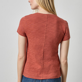 Woman wearing a rust-colored short-sleeve top and blue jeans on a plain background