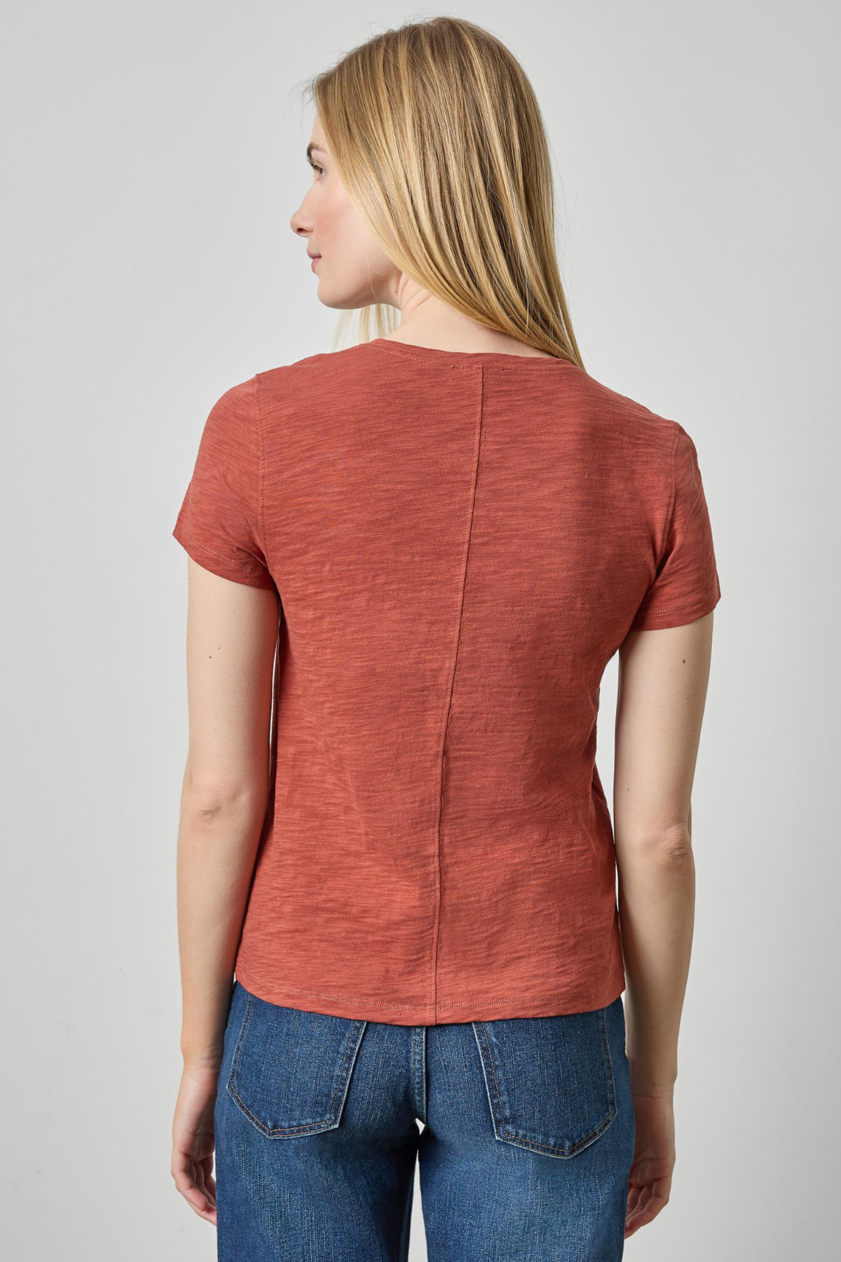 Woman wearing a rust-colored short-sleeve top and blue jeans on a plain background