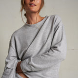 Woman wearing a light grey long-sleeve knit top with a relaxed fit, photographed against a soft neutral backdrop.