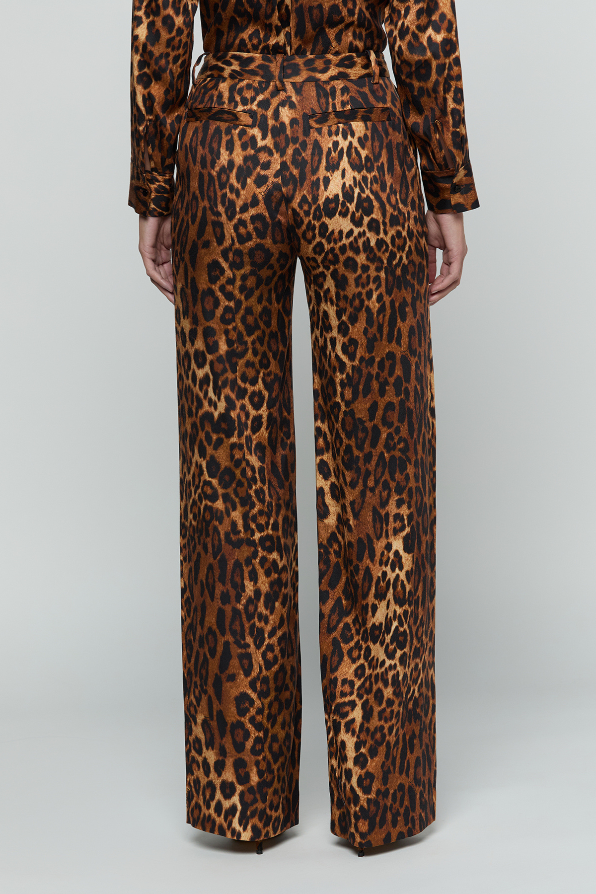 A person shown from the back wearing leopard-print trousers and a matching long-sleeve top against a light gray studio background.