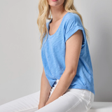 Woman wearing a blue t-shirt and white pants sitting on a white surface with a gray background