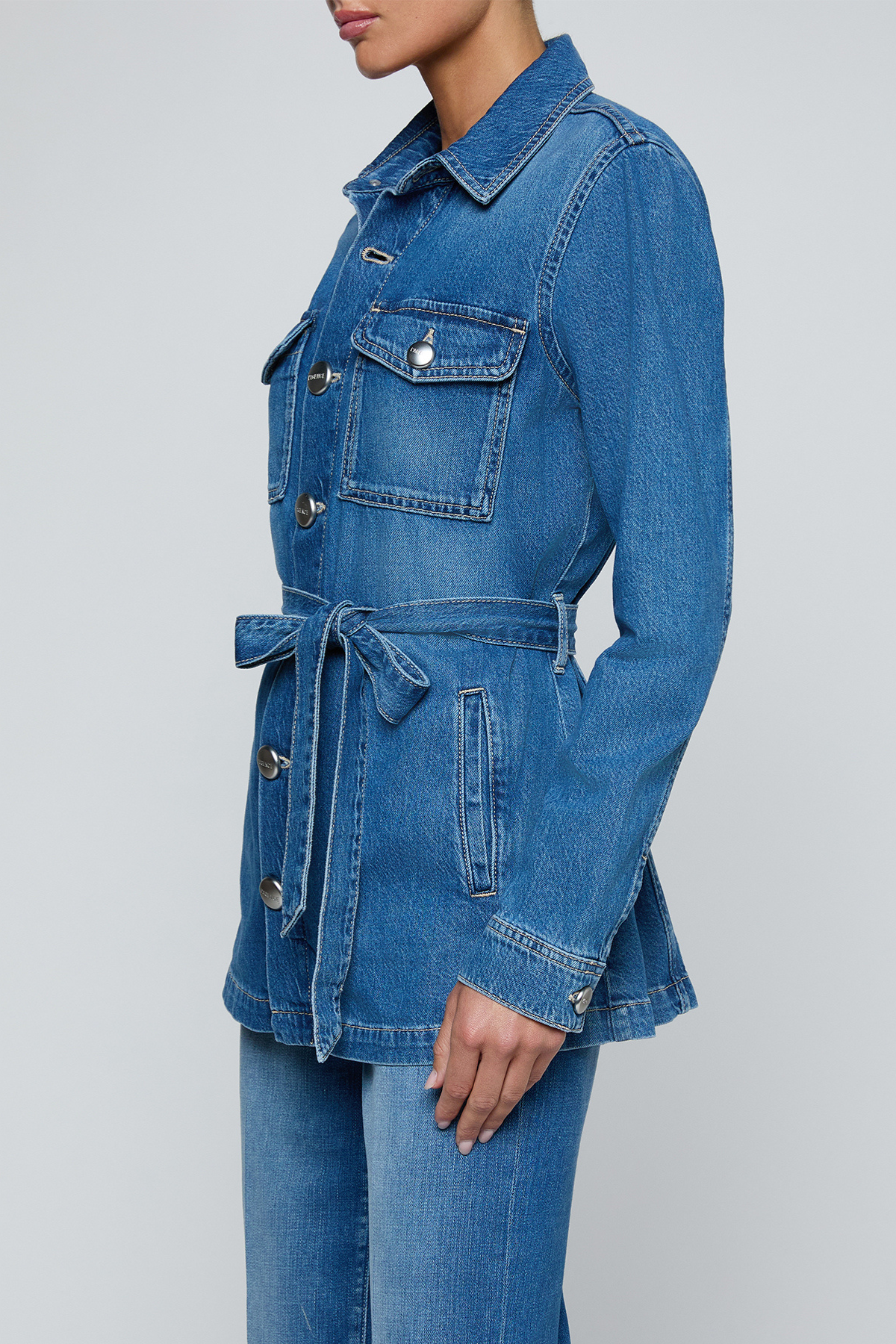 Model wearing a blue denim safari jacket with utility pockets and a button-front design.