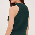 A woman shown from the back wearing a dark green ribbed sleeveless knit top and dark blue jeans against a plain light background.
